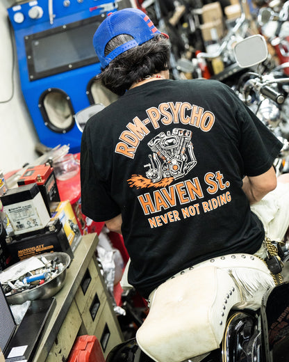 Person wearing a black t-shirt with text sitting on a motorcycle in a workshop.