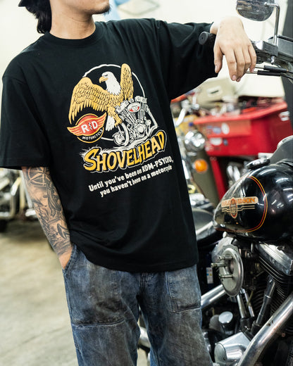 Man wearing a black 'Shovelhead' t-shirt in a garage with motorcycles.